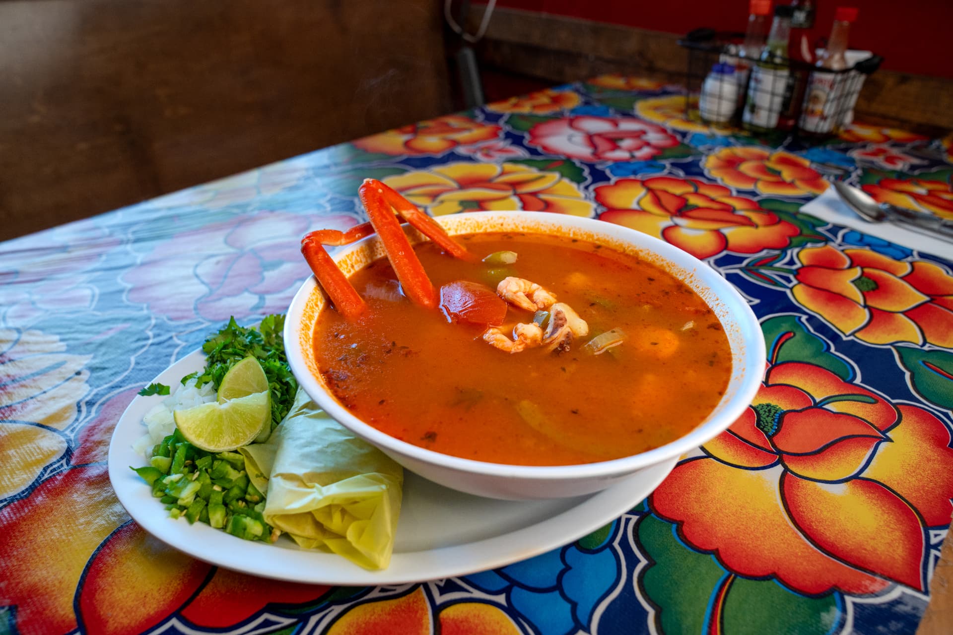 A bowl of caldo de mariscos with crab legs, shrimp, and octopus on a colorful Oaxacan tablecloth